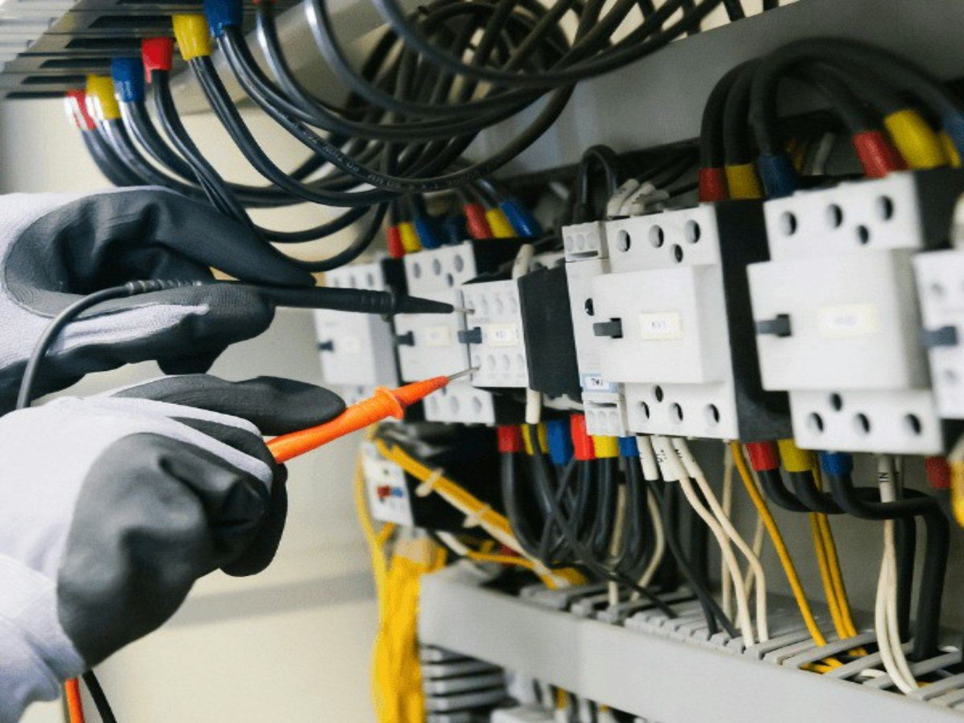 Técnico com luvas testando um quadro elétrico com caneta de teste